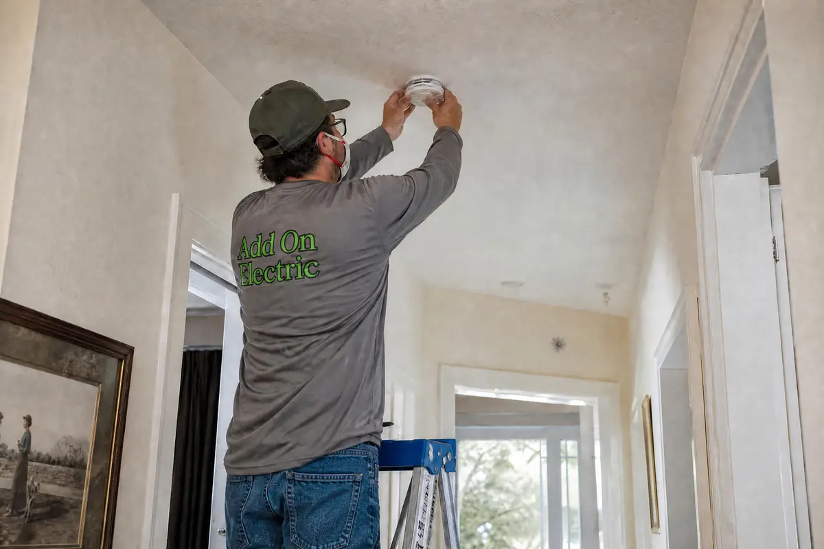 Electrician installing a hardwired smoke detector on a ceiling